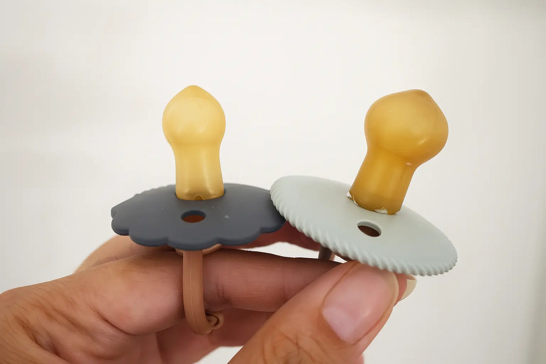 Close-up of two FRIGG natural rubber pacifiers showing size difference due to natural rubber expansion with use. The image illustrates how older pacifiers appear larger than new ones because of softening and material growth.